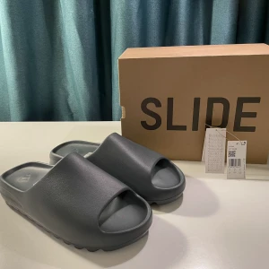 Yeezy Slides Slate Grey - Hej! Säljer ett par DEADSTOCK Yeezy Slides Slate Grey. Strl 50. Köpta på Adidas CONFIRMED. Kvittot och originalbox medföljer.