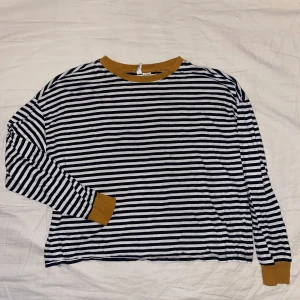 Långärmad tröja  - Svartvit randig tröja med senapsgula detaljer vid händer och hals. Tröjan kommer från H&M och är i storlek L