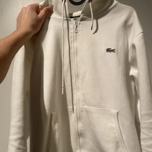 Lacoste zip hoodie  - Vit Lacoste zip hoodie jag vara bara använt den några gången det är en rep den är i bra skick det är storlek S men passar mer som M 