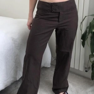 Bruna kostymbyxor - Lågmidjade bruna kostymbyxor med små ränder på från märket NEXT. Storleken är UK 12 men skulle säga att det är en M. Midjemått: 86cm Innerbenslängd: 76cm