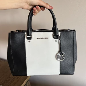 Michael Kors väska - Vit/svart axelväska från Michael Kors. Den Jag har två stora fack på varsin sida med dragkedja. Fyra små fack och ett med dragkedja inuti. Använd men fortfarande i fint skick.   Inköptes för ca 2500kr säljer för 500kr. 