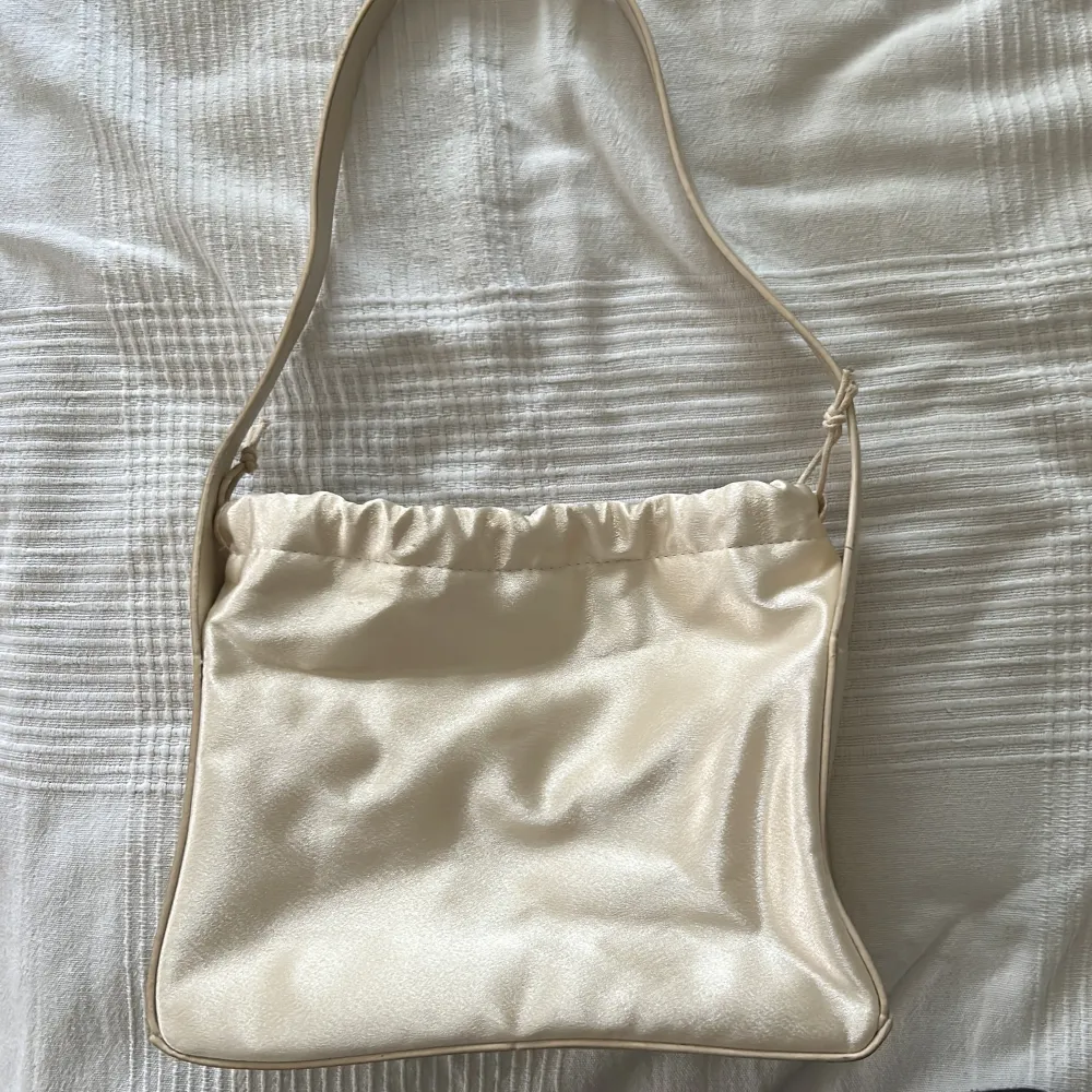 säljer denna väska i fin ljusbeige/créme silk ish material 🤍 materialet är i bra skick då jag knappast använt den :)‼️köpare står för frakten!. Väskor.