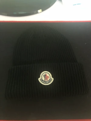 Äkta Moncler mössa - Hej, jag säljer en äkta Moncler mössa som jag fick i julklapp men har inte haft någon användning för den och tänkte att de är smartare att sälja den istället för att den ska samla massa damm.  Den får plats på ett normalt huvud kanske inte ett litet barn.