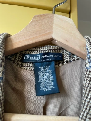 Blazer Ralph Lauren - Jättefin blazer från Ralph Lauren i tweed. Beiga grundtoner men med ett ljusblått stråk. En knapp är sönder men tre originalknapper medföljer och kan lätt bytas ut. 
