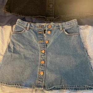 Jeansskjol - Jeanskjolar från Monki. Ena svart med svarta knappar och den andra blå med bronsfärgade knappar💓 En för 89kr eller båda för 170kr✨ Båda strl 38!