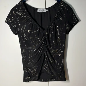 T-shirt Louiza - T-shirt från märket Louiza köpt second hand. Räfflad i mitten med coolt metalliskt tryck, syns nog lite dåligt i bilden. Fint skick. Har aldrig blivit använd. Storlek: S