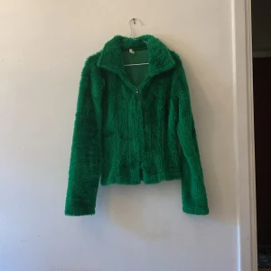 Jacka / kofta - Grön fluffig jacka med dragkedja. fakepäls. Svårt att fånga färgen på kameran men sista bilden är direkt solljus och de andra två är utan direkt solljus