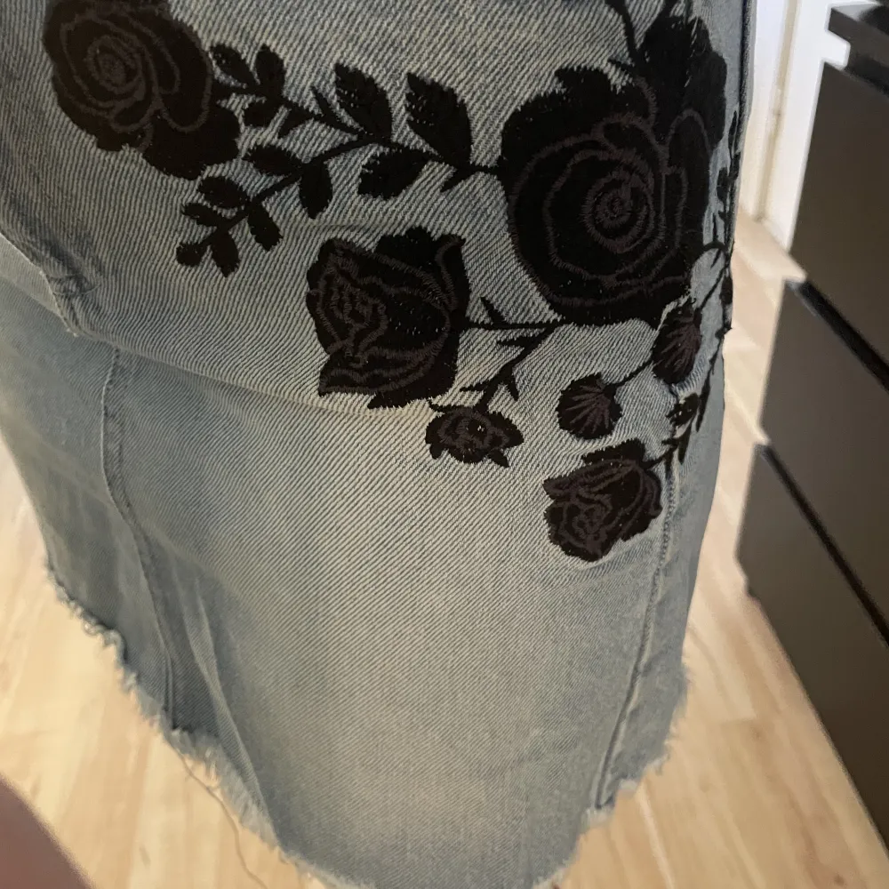 Säljer en jeanskjol med broderade svarta blommor på sidan. Köpt från NA-KD i storlek 34🫶🏼. Kjolar.