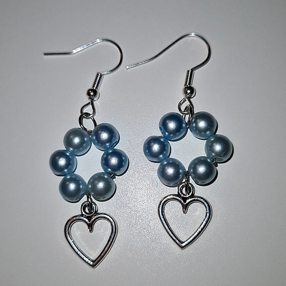 Ett par handgjorda blå-blomformade örhängen med ett varsitt hängande hjärta nedtill. Ej äkta silver så kan innehålla nickel. . Accessoarer.