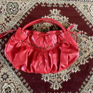 röd handväska med åtsnörning upptill för att variera väskan längd. coola nitar på framsidan, dragkedja för att stänga och två extra fack inuti. 
