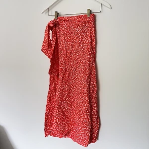 röd kjol med vita blommor - röd kjol med vita blommor på och knytdetalj från monki i strlk xxs. fladdrar fint och sitter på bra. 