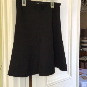 Svart kjol från Oodji - Snygg svart kjol från Oodji med en klassisk design. Kjolen har en enkel och stilren look som passar perfekt till olika tillfällen. Den är tillverkad i ett mjukt material som ger en bekväm passform.