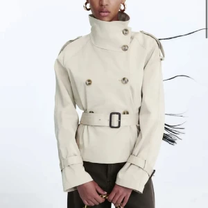 Beige trenchcoat med bälte - Snygg beige trenchcoat med hög krage och knappar. Köpt på plick men är i nyskick! Säljer då den inte riktigt passade mig❤️slutsåld på hemsidan