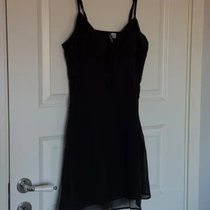 Svart klänning från H&M - Snygg svart klänning från H&M med smala axelband och knytning framtill. 