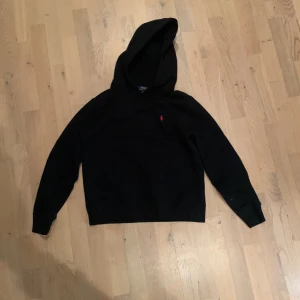 Svart hoodie från Ralph Lauren - Säljer en stilren svart hoodie från Ralph Lauren med en liten röd logga på bröstet. Perfekt för en avslappnad look. Den har en klassisk huva och långa ärmar. Pris kan diskuteras!