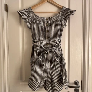 Randig offshoulder one piece från Amisu - Säljer en snygg randig one piece från Amisu i offshoulder-stil. One piecen har korta ärmar och ett knytbälte i midjan för en fin passform. Perfekt för varma dagar!