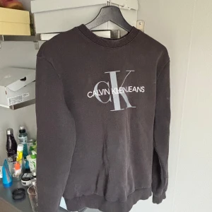 Svart tröja från Calvin Klein Jeans - Säljer en stilren svart tröja från Calvin Klein Jeans med deras ikoniska logga i vitt på framsidan. Tröjan har en normal passform och är perfekt för en avslappnad look. Den är tillverkad i ett mjukt material som ger en skön känsla.