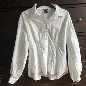 Vit skjorta från Lindex - Säljer en klassisk vit skjorta från Lindex med ballongärm och intagen midja. Aldrig kommit till användning så prislappen är kvar.
