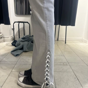 Grå jeans med snörning - Snygga grå jeans med snörning längs sidorna. De har en straight/flare passform. Frakten är inkluderad i priset! 
