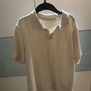 Vit pikétröja - Säljer en stilren vit pikétröja med korta ärmar. Perfekt för en avslappnad och klassisk look. Tröjan har en krage och är tillverkad i ett lätt och luftigt material.