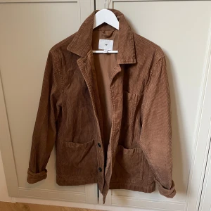 Brun manchesterjacka - Säljer en snygg brun manchesterjacka med klassisk krage och knappar framtill. Jackan har två stora fickor och långa ärmar. Perfekt för höst och vår!