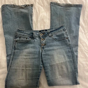 Blå jeans med knappar - Snygga blå jeans med en klassisk look och knappar framtill. De har en bootcut-stil och är perfekta för en avslappnad stil. Fickor både fram och bak ger en praktisk touch.