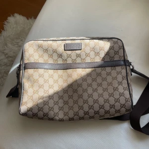 Gucci axelväska - Schysst axelväska i beige och brunt med ett klassiskt mönster. Väskan har en justerbar axelrem och en dragkedja för säker förvaring. Finns extra fack i väskan för pennor, miniräknare osv. Perfekt för plugget! 