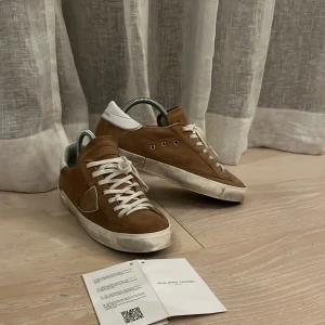 Bruna sneakers från Philippe Model storlek 40  -  Intressekoll !!!!! Snygga bruna sneakers från Philippe Model  med vita detaljer och snörning. Skorna har en klassisk design med en logotyp på sidan och en vit sula. Perfekta för en stilren look. Pris kan sänkas vid prisförslag 