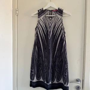 Mönstrad ärmlös klänning från Indiska - Snygg ärmlös klänning från Indiska med ett unikt svartvitt mönster. Klänningen har en elegant design med rund hals och dragkedja i ryggen. (Katt o kanin finns i hemmet)