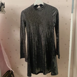 Svart glittrig klänning - Snygg svart glittrig klänning med långa ärmar och en liten öppning i ryggen. Perfekt för en kväll ute eller en festlig tillställning. Storlek XS/S