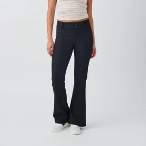 Svarta flare kostymbyxor - Snygga svarta flare kostymbyxor med lågmidja och knappar. Byxorna har fickor med knappdetaljer baktill och är perfekta för en stilren look. Passar bra till både vardag och fest.