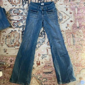 Lågmidjade jeans - As snygga jeans från Nelly med fickor och detaljer framtill, för långa (därför nötta längst ner på baksidan - se bilder), använda men i bra skick, lågmidjade / mid rise, stretchigt material. Bredd ca 32 cm, längd ca 105 cm, innerbenslängd ca 82 cm.