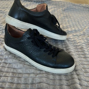 Svarta sneakers med snörning - Snygga svarta sneakers i skinn med snörning och vit sula. Perfekta för en stilren look. De har en klassisk design med rund tå och är bekväma för vardagsbruk.