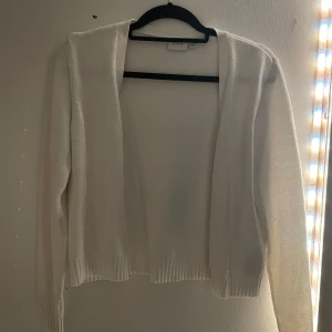 Vit kofta från VILA - Säljer en stilren vit kofta från VILA. Koftan har långa ärmar och ribbade kanter vid ärmslut och nederkant. Perfekt för lager-på-lager under kyligare dagar. Passar till många olika outfits!