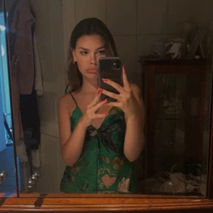 Grön blommig klänning - Säljer en grön klänning med blommigt mönster och smala axelband. Klänningen har en v-ringad design med knytning framtill och är perfekt för sommarens varma dagar. Väldigt smickrande passform!🍏💚