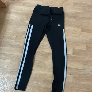 Svarta träningsleggings med vita ränder - Snygga svarta träningsleggings från 157 med vita ränder längs sidorna. Perfekta för gymmet eller löprundan. De har en tight passform och är tillverkade i ett stretchigt material för maximal komfort.