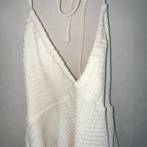 Vit Sommartopp med v-ringning - Säljer en stilren vit sommartopp med v-ringning och smala axelband. Den har en texturerad yta och en luftig passform som ger en avslappnad look. Perfekt för varma dagar! Eller bör du åker till stranden🌊☀️🏖️
