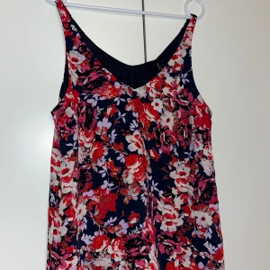 Toppi - Naisten kiva kesäinen toppi, jossa punertavis kukkia. Koko L.  Kaikai n 47cm olkahelma n 62cm. Kissatalous MMM Mikäli hinta ei miellytö tarjoa rohkeasti Katsothan myös muut ilmoitukseni!!