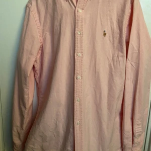 Rosa skjorta från Polo Ralph Lauren - Säljer en stilren rosa skjorta från Polo Ralph Lauren i slim fit. Skjortan är perfekt för sommaren. Den är broderad med det klassiska Polo Ralph Lauren-logotypen på bröstet. Perfekt för en elegant look!