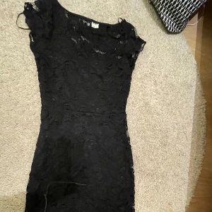 Svart spetsklänning från H&M Divided - Snygg svart spetsklänning från H&M Divided. Klänningen har ett vackert spetsmönster och korta ärmar. Perfekt för en elegant kvällslook. Den är figurnära och har en klassisk design som aldrig går ur stil.