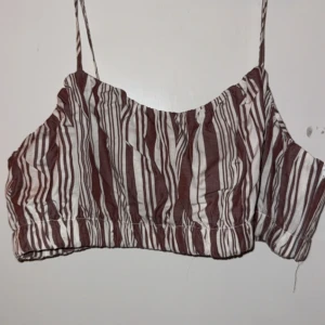 Randig linnetopp från H&M - Säljer en randig linnetopp från H&M i brunt och vitt. Toppen har smala axelband och en croppad passform, perfekt för varma dagar. Materialet är lätt och luftigt, vilket gör den bekväm att bära.💕🤩