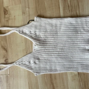 Beige ribbad linnetopp från H&M - Säljer en stilren beige ribbad linnetopp från H&M. Toppen har smala axelband och en v-ringad design som ger en elegant look. Perfekt för varma dagar eller som ett lager under en jacka.