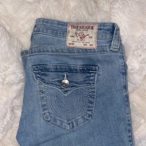 Blå jeans från True Religion - Säljer ett par snygga blå jeans från True Religion med låg midja och flare-stil. De har en klassisk femficksdesign och en dekorativ bakficka med knapp. Köpta i februari för 1300kr men kommer aldrig till användning. Nuddar marken på mig som är 171.❤️ 