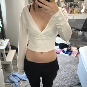 Vit omlottopp från ONLY - Säljer en stilren vit omlottopp från ONLY. Toppen har en v-ringad design och är långärmad med en ribbad struktur. Perfekt för en chic och bekväm look.