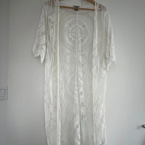 Vit spets från Lindex S/M - Superfin vit lång utanpå”kofta”från Lindex i transparent spets med broderade mönster och vida ärmar. Perfekt för sommaren med sitt luftiga material och snygga detaljer. Klänningen har ett boho-inspirerat uttryck och är riktigt unik.