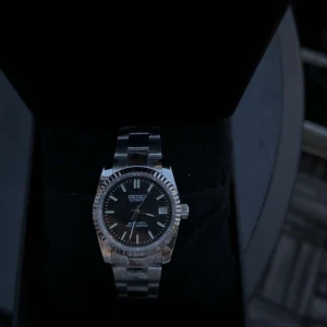Seiko automatisk klocka i silver - Stilren Seiko automatisk klocka med svart urtavla och datumvisning. Klockan har en robust länk i silverfärgat stål och markerade index. Perfekt för dig som gillar klassisk och tidlös design med en sportig touch.