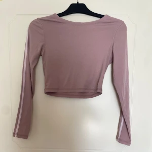 Ljusrosa croppad topp från BikBok - Säljer en ljusrosa croppad långärmad topp från BikBok. Toppen har en enkel design med en smal vit rand längs ärmarna och är tillverkad i mjuk bomullsmix. Perfekt för dig som gillar en sportig och stilren look.
