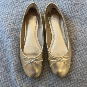 Guldiga ballerinaskor från H&M - Snygga ballerinaskor i metallic guld från H&M. Använda ett fåtal gånger och i bra skick 