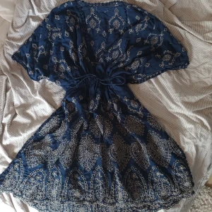 Bikini cover-up - Supersöt marinblå kortklänning med vita broderier och spetsdetaljer. Klänningen har vida korta ärmar, markerad midja med knyt och vackert mönster över hela tyget. Öppen på båda sidan av benen, vet inte märket då jag köpte den secondhand och lappen är utsuddad