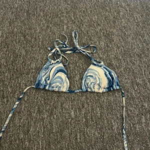 Blåvit bikiniöverdel med knyt - Snygg bikiniöverdel i blått och vitt med swirl-mönster. Klassisk trekantsmodell med knyt både i nacken och runt ryggen. Perfekt för stranden eller poolen, ger en fräsch och trendig look.